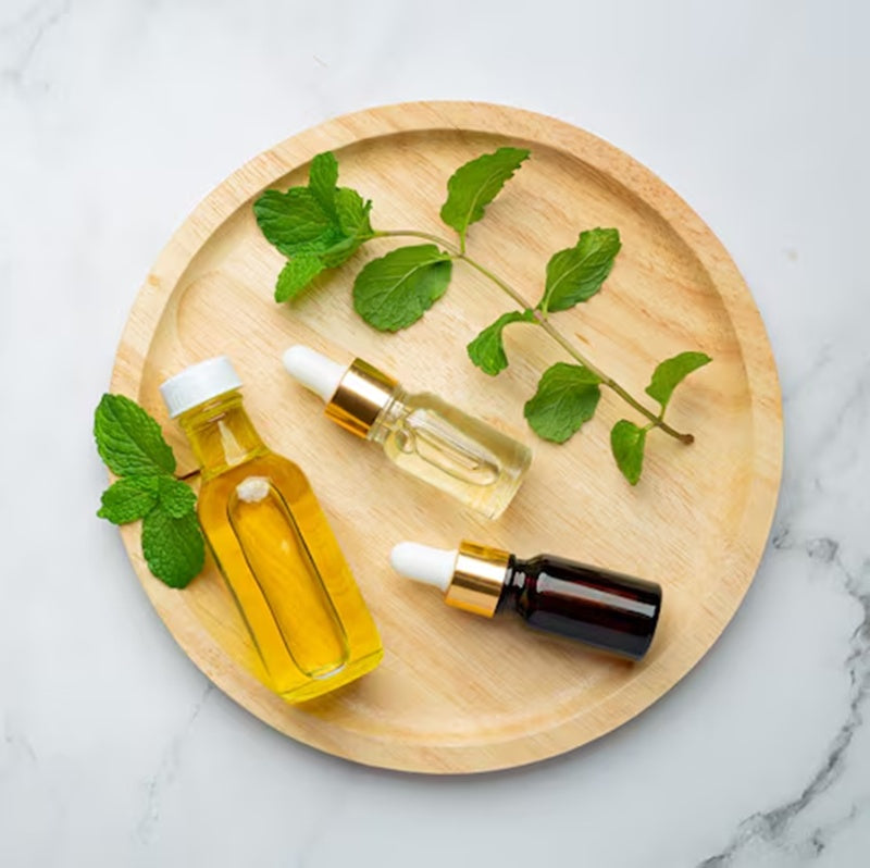 assorted oils on a wooden plate with fresh cut herbal leaves