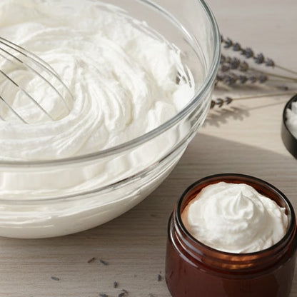 Whipped cream in a glass bowl and jar on a wooden surface with lavender flowers.